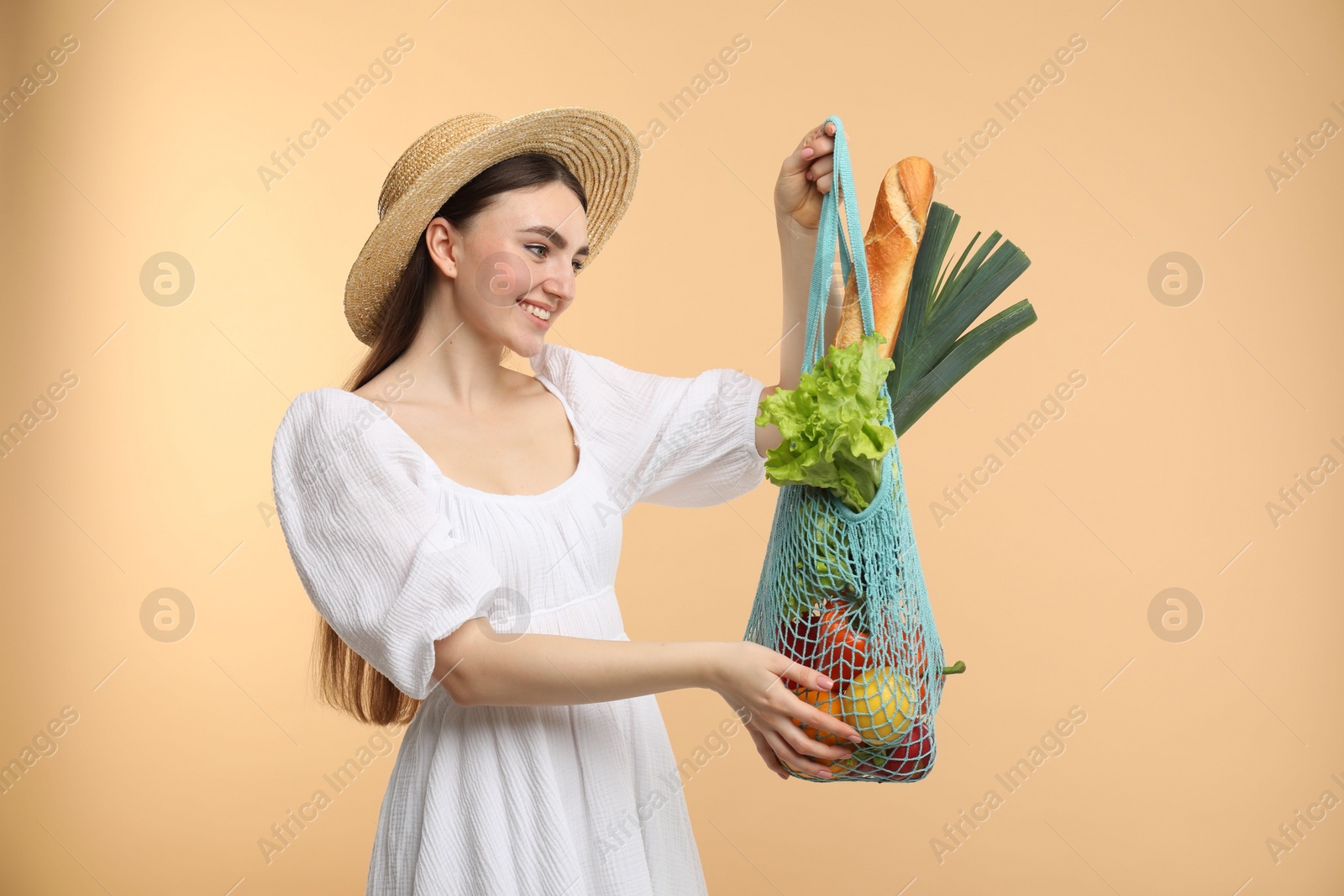 Photo of Woman with string bag of fresh vegetables and baguette on beige background