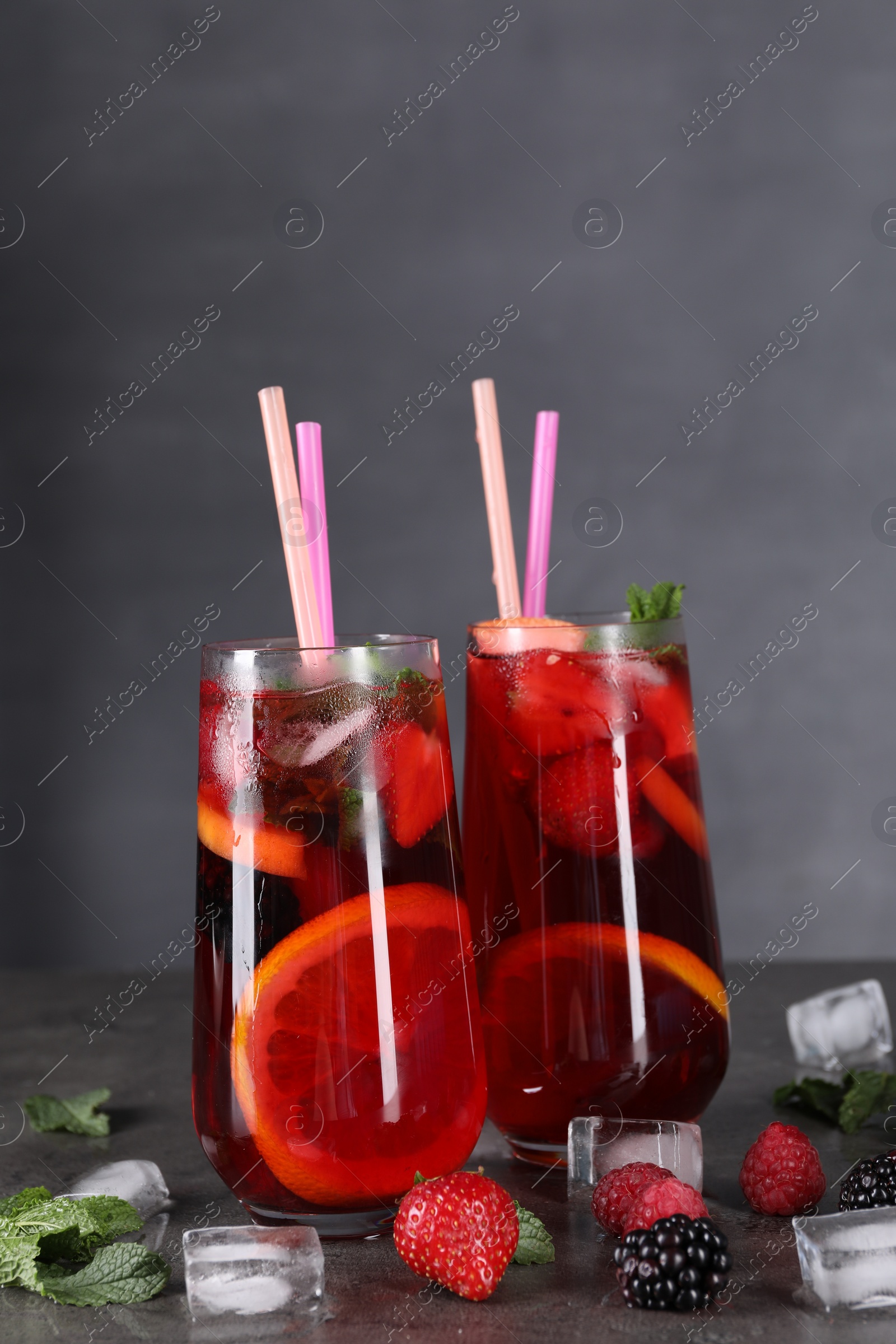 Photo of Delicious refreshing sangria, ice cubes and berries on grey table