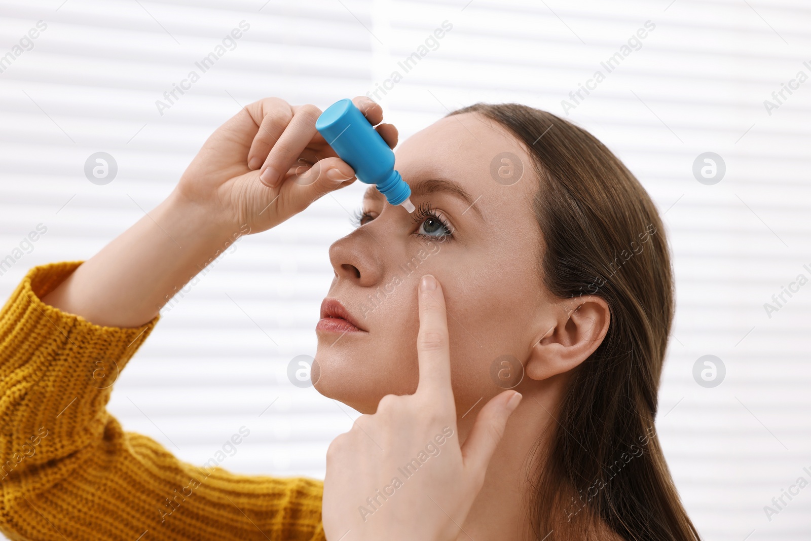 Photo of Young woman applying medical eye drops indoors, closeup