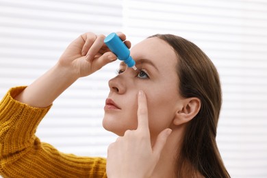 Young woman applying medical eye drops indoors, closeup