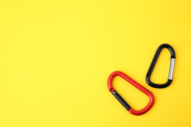Two metal carabiners on yellow background, flat lay. Space for text