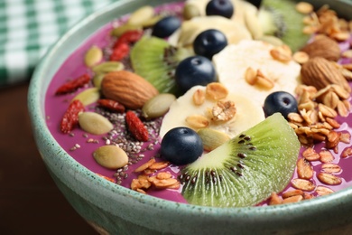 Delicious acai smoothie with granola and fruits in bowl on table, closeup