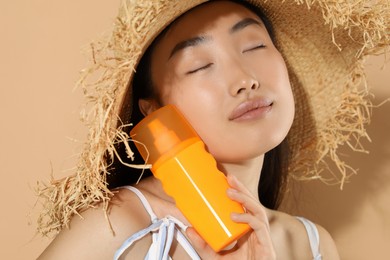 Photo of Beautiful young woman in straw hat holding sun protection cream on beige background, closeup