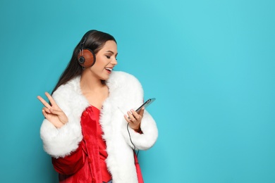 Young woman in Santa costume listening to Christmas music on color background