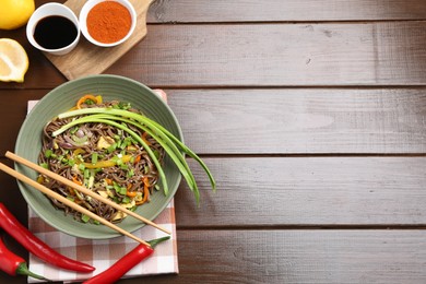 Photo of Stir-fry. Delicious cooked noodles with chicken and vegetables in bowl on wooden table, flat lay. Space for text