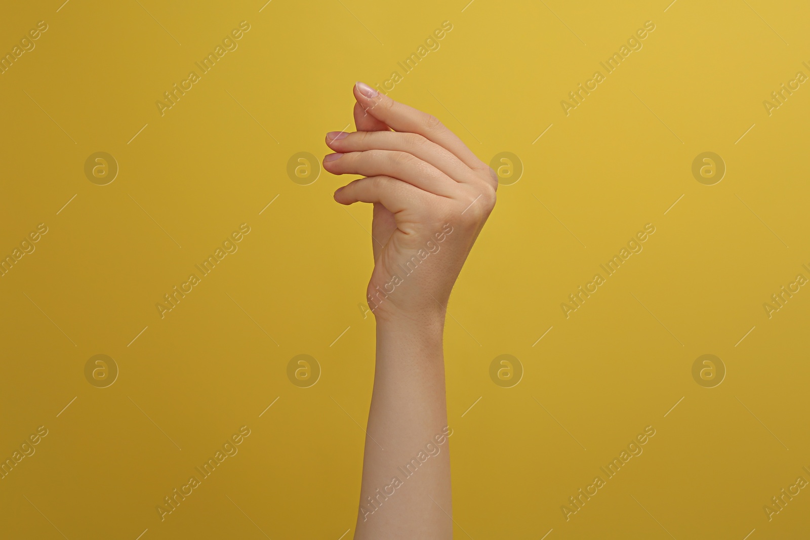 Photo of Woman showing thumb and index finger together on yellow background, closeup