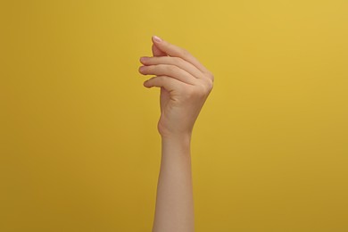 Photo of Woman showing thumb and index finger together on yellow background, closeup