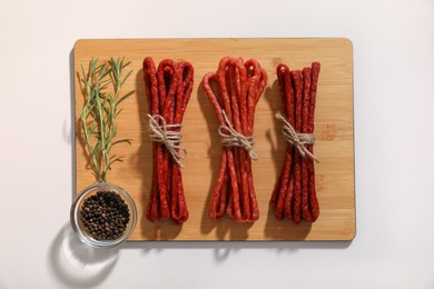 Photo of Bundles of delicious kabanosy with peppercorn and rosemary on white background, top view