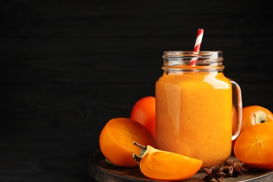 Tasty persimmon smoothie with straw and fresh fruits on table against black background. Space for text