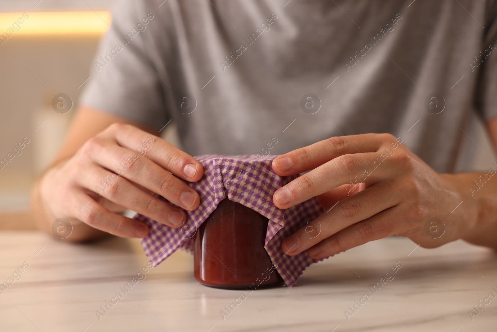 Photo of Man packing jar of jam into beeswax food wrap at light table indoors, closeup