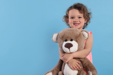 Cute little girl with teddy bear on light blue background, space for text