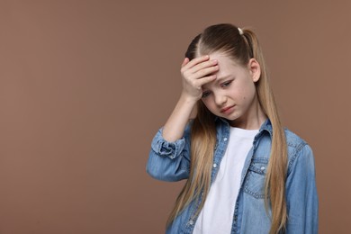 Photo of Little girl suffering from headache on brown background. Space for text