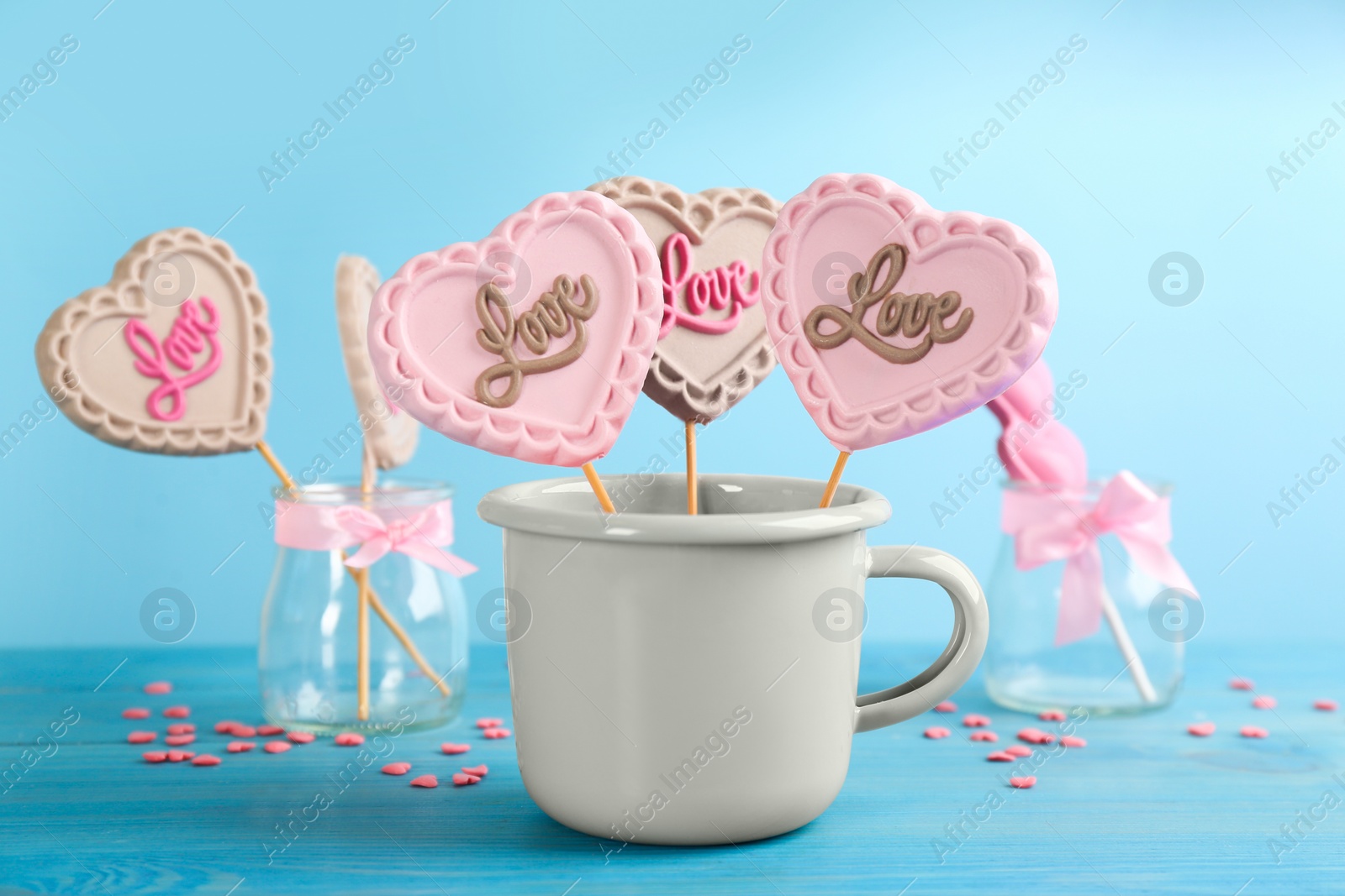 Photo of Heart shaped lollipops made of chocolate in cup and sprinkles on light blue background