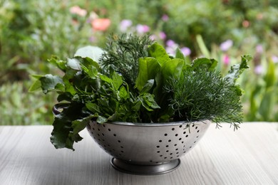 Photo of Different herbs in colander on white wooden table outdoors