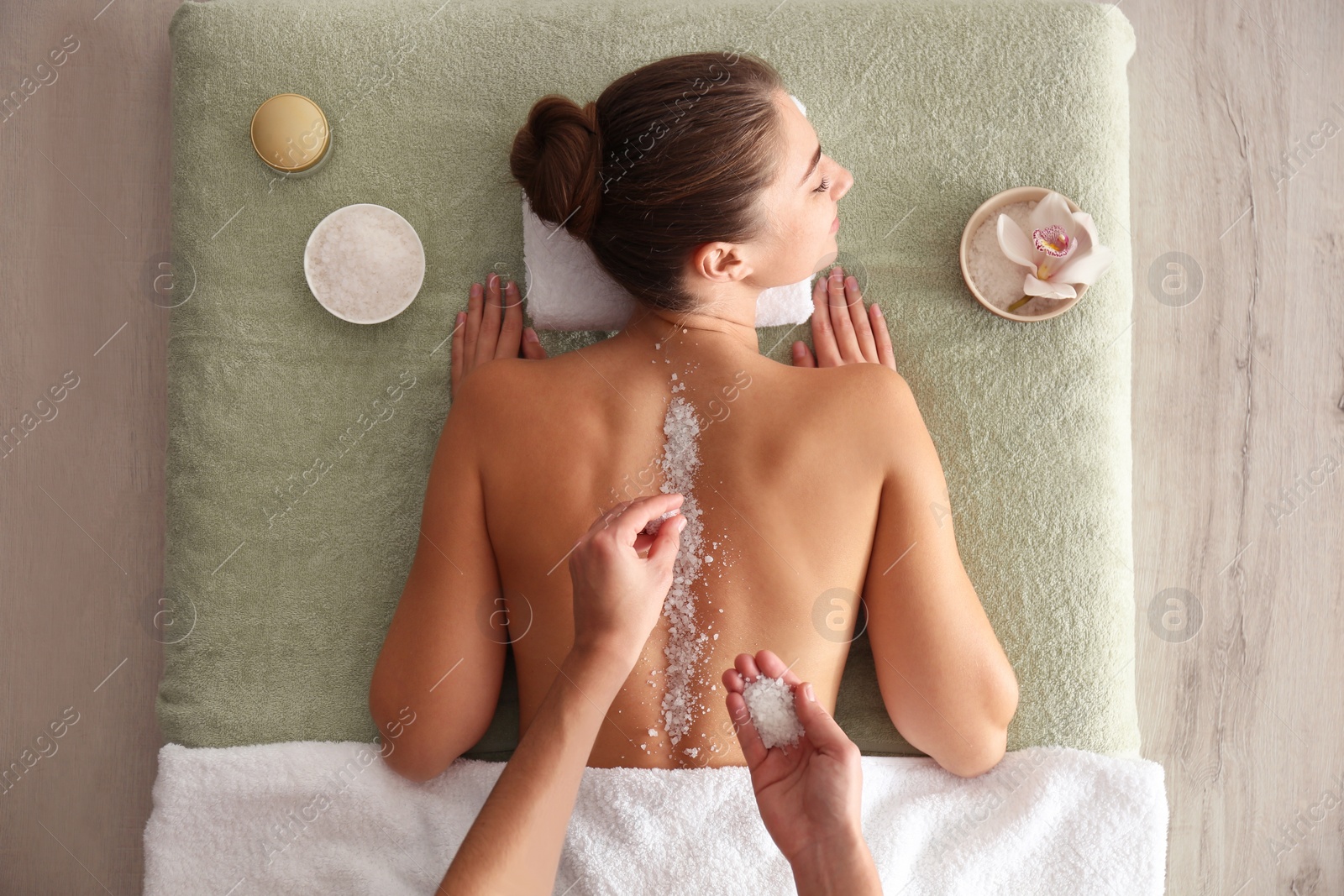 Photo of Young woman having body scrubbing procedure with sea salt in spa salon, top view