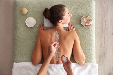 Young woman having body scrubbing procedure with sea salt in spa salon, top view
