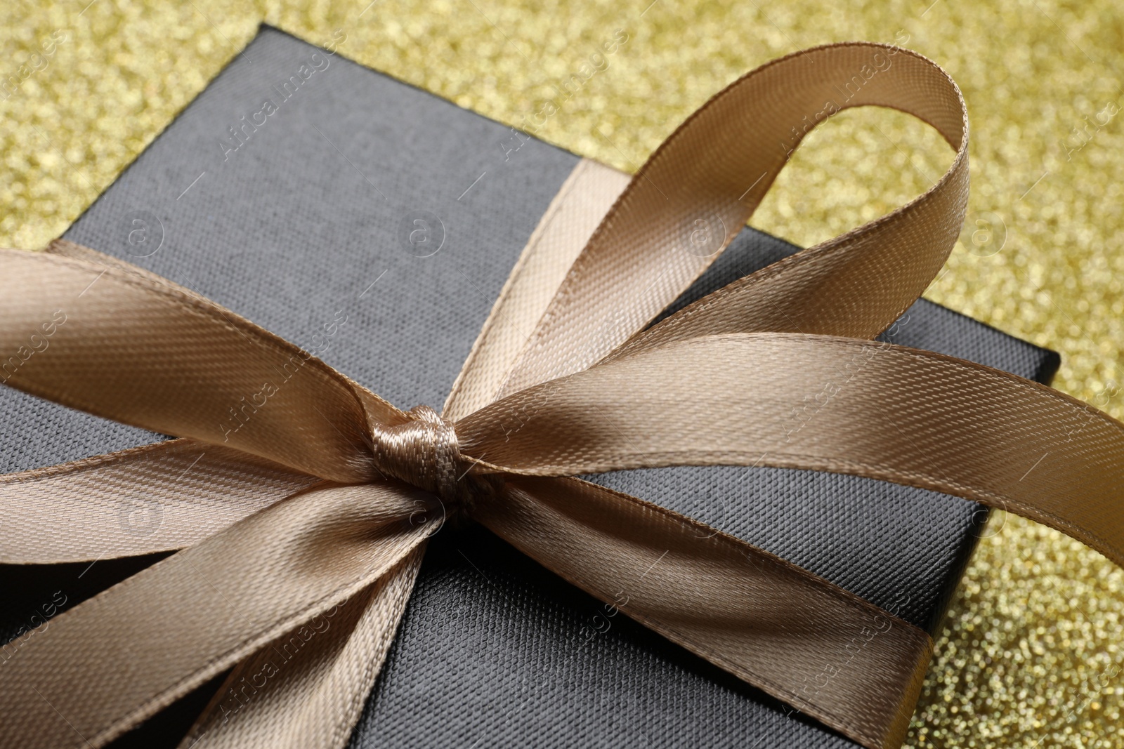 Photo of Gift box with golden bow on shiny background, closeup
