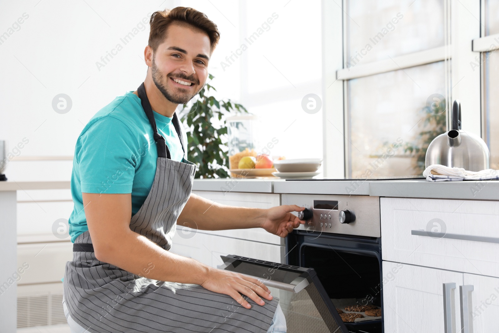 Photo of Young man baking cookies in oven at home