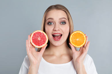 Photo of Emotional young woman with cut orange and grapefruit on grey background. Vitamin rich food