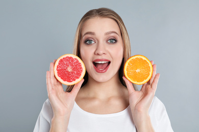 Emotional young woman with cut orange and grapefruit on grey background. Vitamin rich food