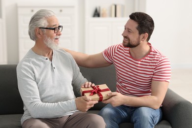 Photo of Son giving gift box to his dad on sofa at home