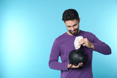 Photo of Happy young man putting money into piggy bank on color background. Space for text