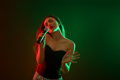 Beautiful woman with microphone singing in color lights on dark background. Space for text