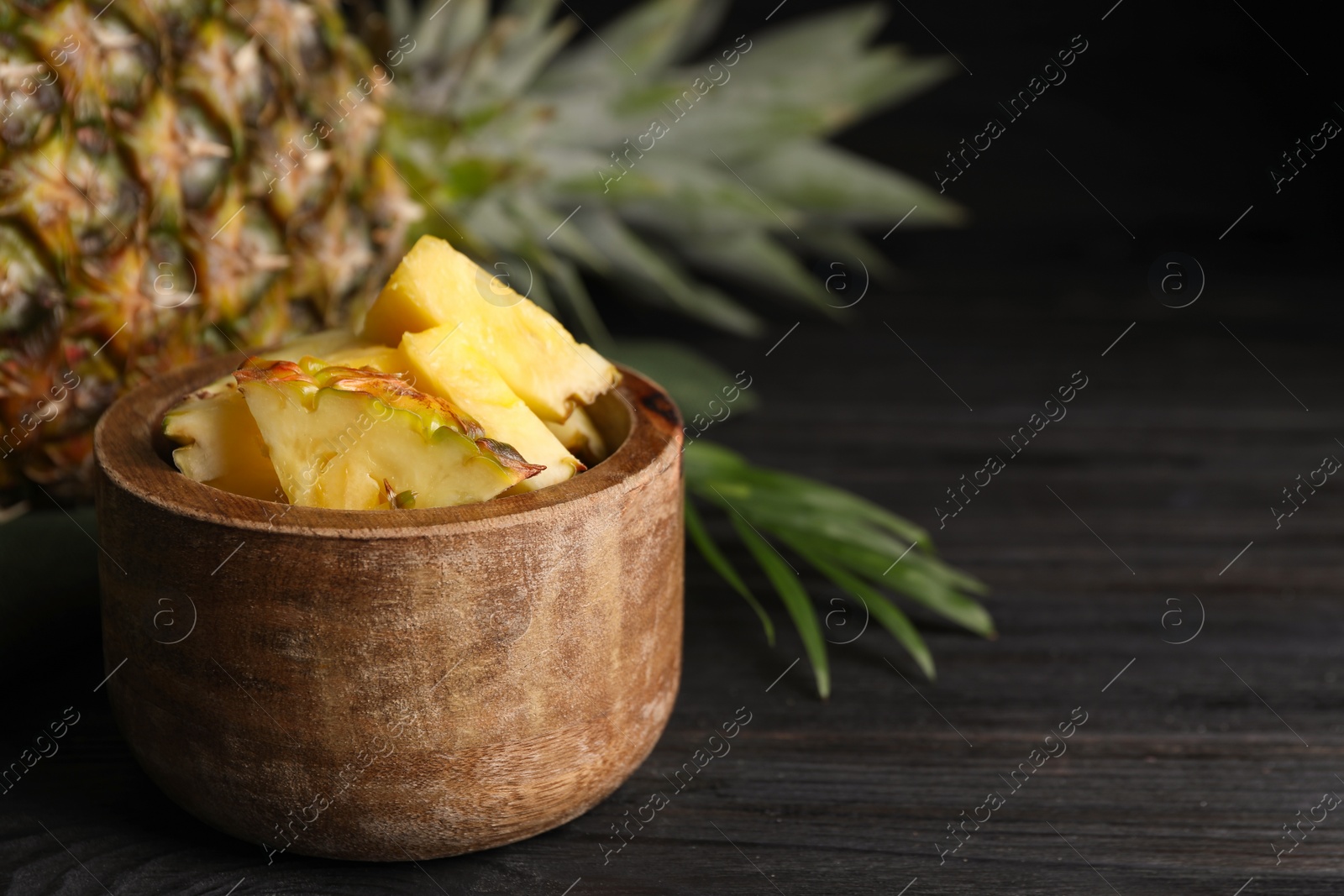 Photo of Pieces of tasty ripe pineapple in bowl on dark wooden table. Space for text