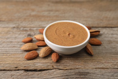 Delicious nut butter in bowl and almonds on wooden table, closeup