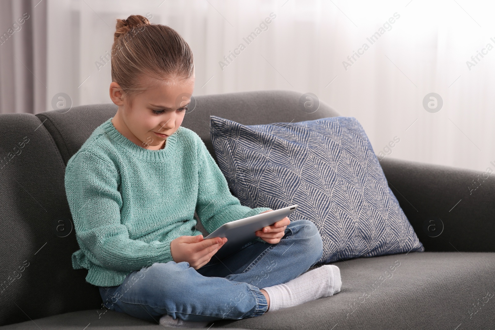 Photo of Little girl using tablet on sofa at home. Internet addiction