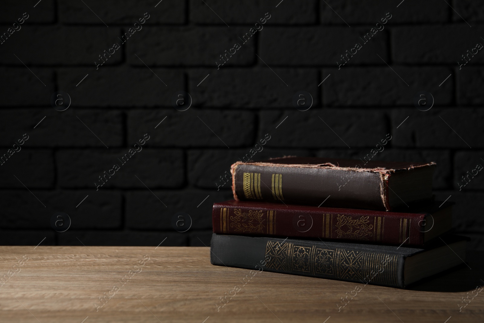 Photo of Stack of old hardcover books on wooden table near black brick wall, space for text