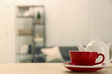 Photo of Red cup and saucer on wooden table in room, space for text