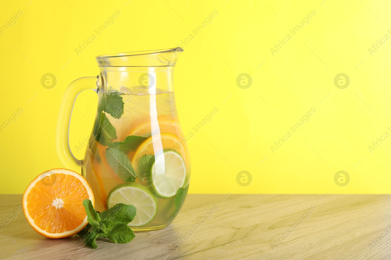 Photo of Freshly made lemonade with mint in jug on wooden table against yellow background, space for text