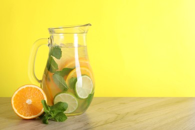 Freshly made lemonade with mint in jug on wooden table against yellow background, space for text