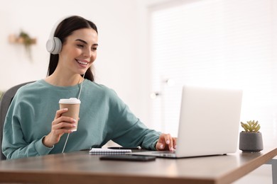 Young woman in headphones watching webinar at table in room