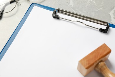 Photo of Clipboard with blank sheet of paper and wooden stamp on light grey table, closeup