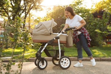 Photo of Happy mother with baby in stroller walking in park on sunny day