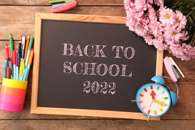 Back to school 2022. Blackboard, stationery, alarm clock and flowers on wooden table, flat lay