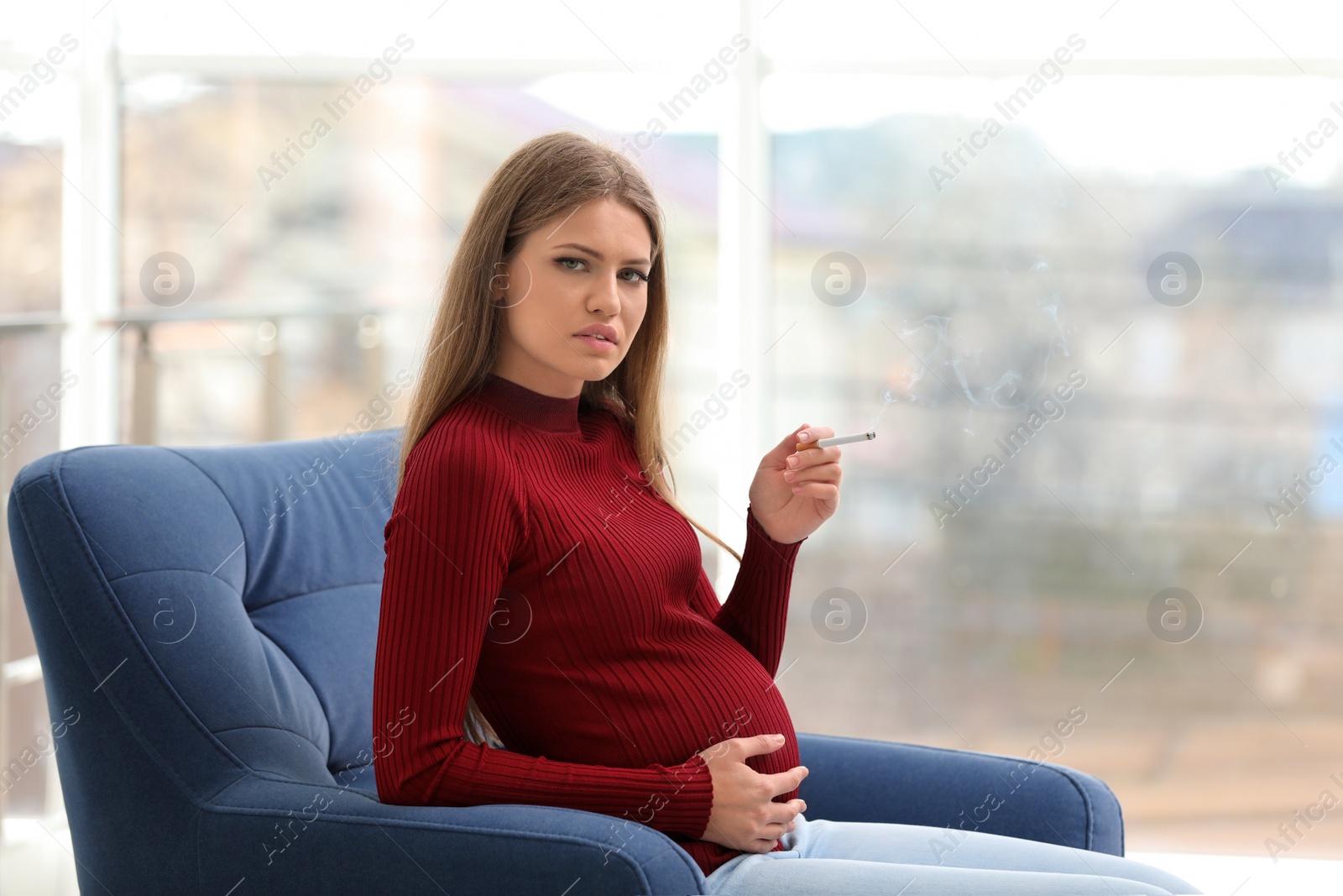 Photo of Young pregnant woman smoking cigarette at home. Harm to unborn baby