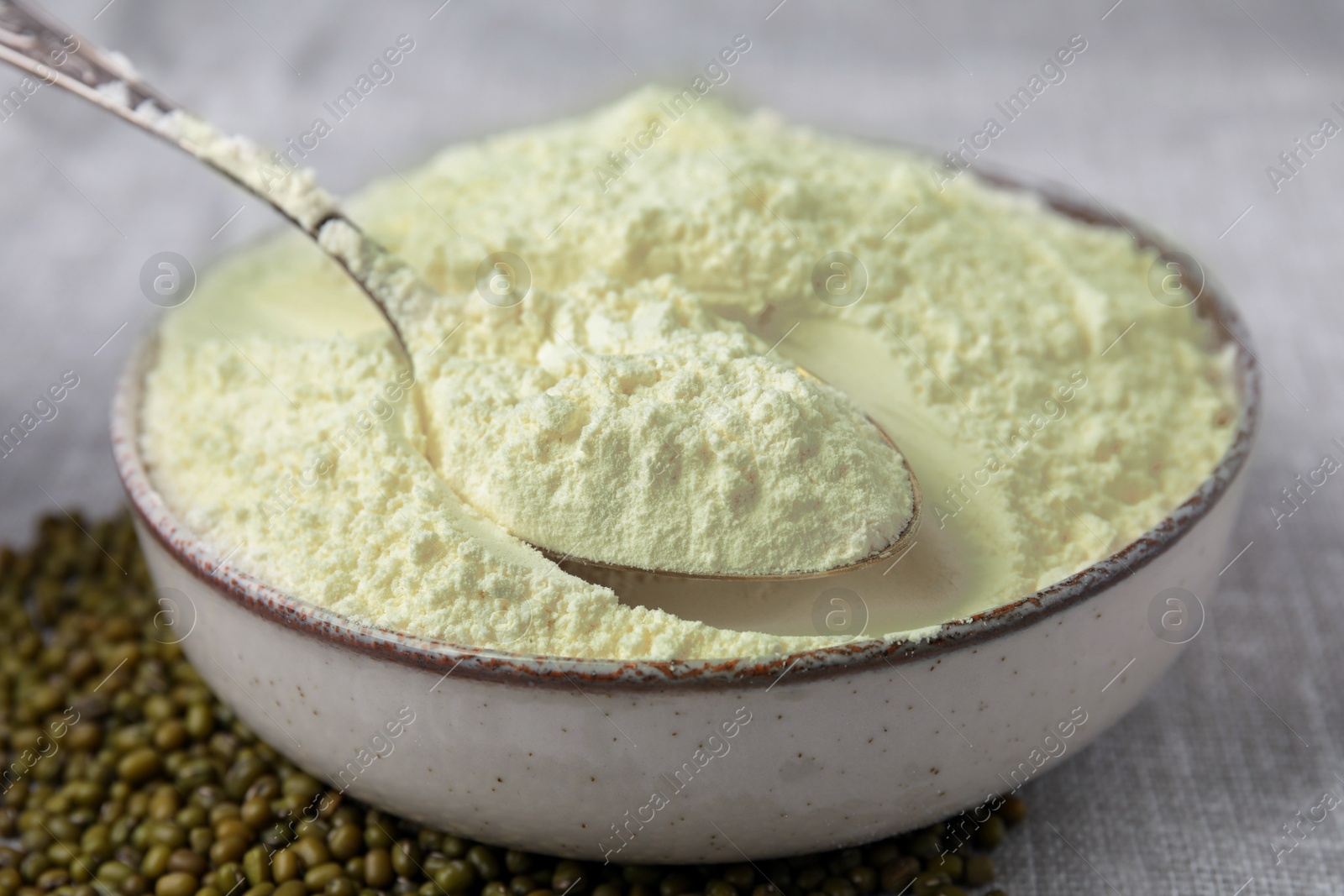 Photo of Bowl of flour, spoon and mung beans on light grey cloth, closeup