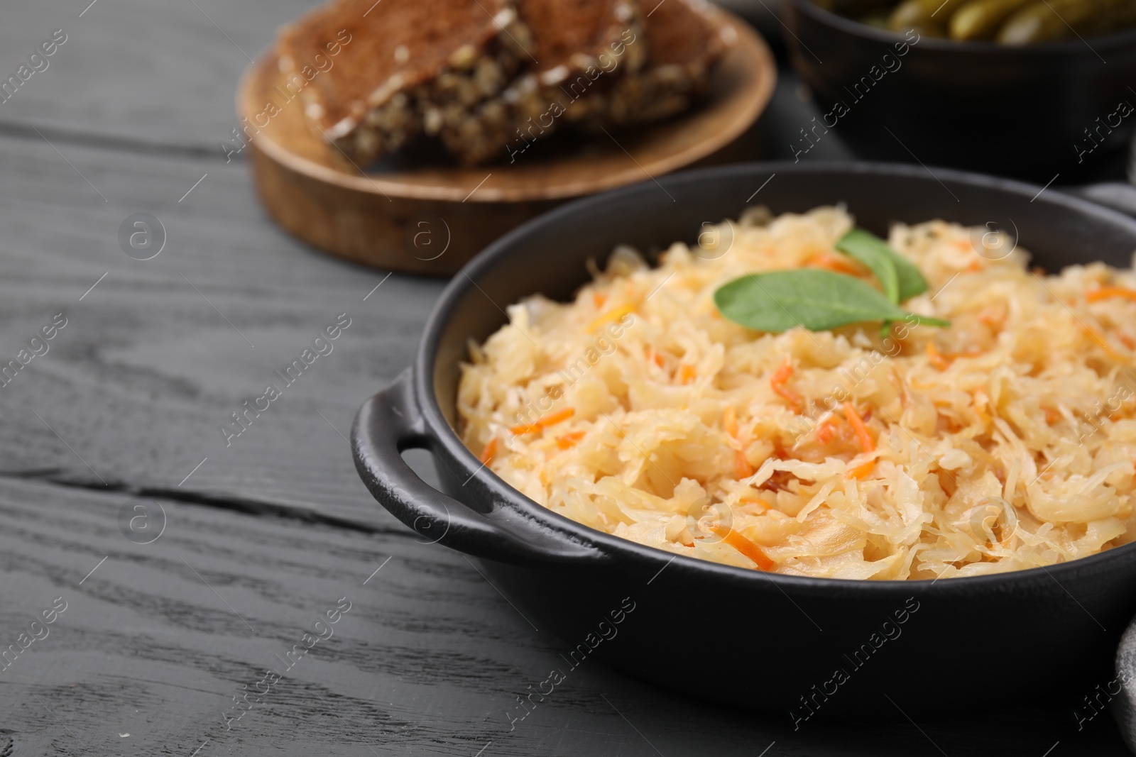 Photo of Serving pan with sauerkraut on black wooden table, closeup. Space for text