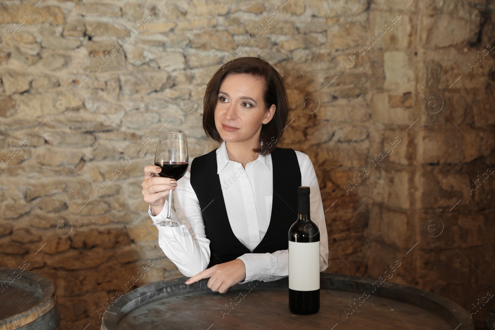 Photo of Female sommelier with glass of red wine at table indoors