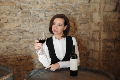 Photo of Female sommelier with glass of red wine at table indoors