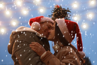 Photo of Happy couple kissing under mistletoe bunch outdoors in snowy evening, low angle view