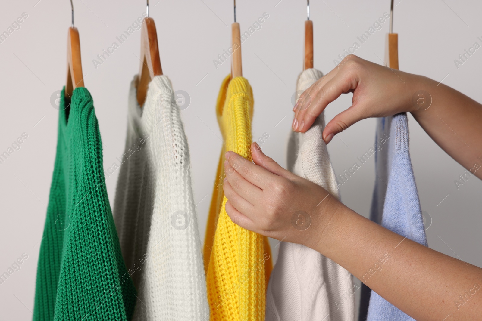 Photo of Woman taking knitted sweater on light background, closeup