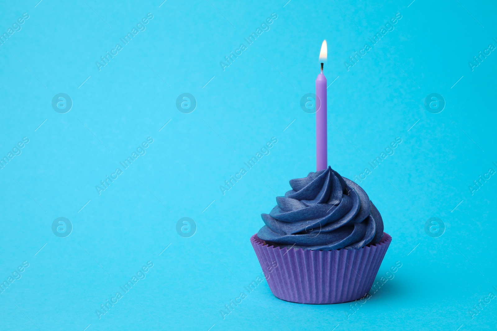 Photo of Delicious birthday cupcake with burning candle on light blue background. Space for text