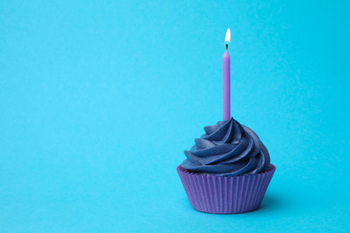 Photo of Delicious birthday cupcake with burning candle on light blue background. Space for text