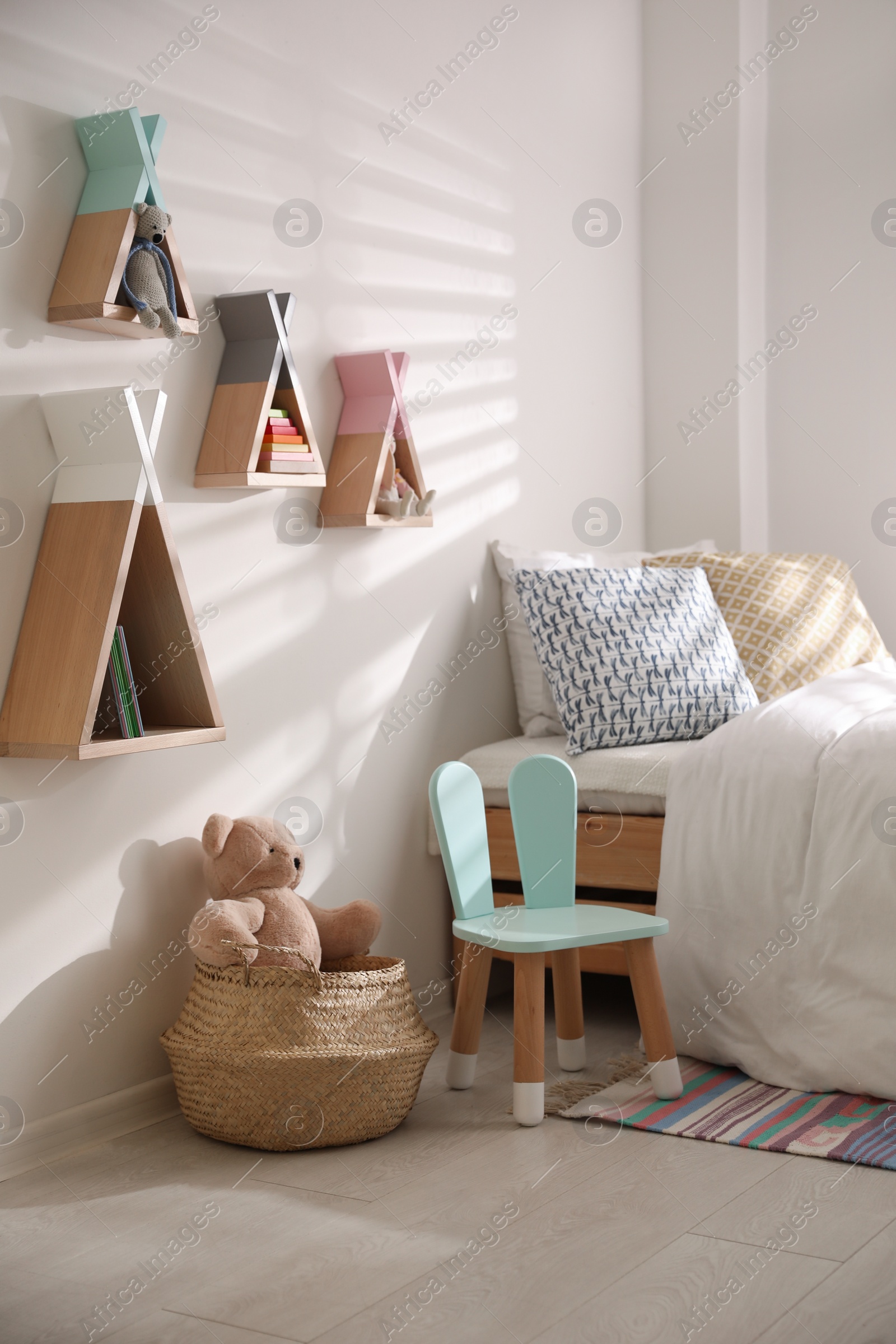 Photo of Cute little chair with bunny ears near bed indoors. Children's room interior