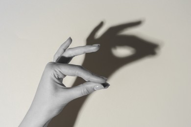 Shadow puppet. Woman making hand gesture like llama on light background, closeup. Black and white effect