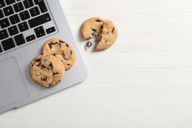 Chocolate chip cookies and laptop on white wooden table, flat lay. Space for text